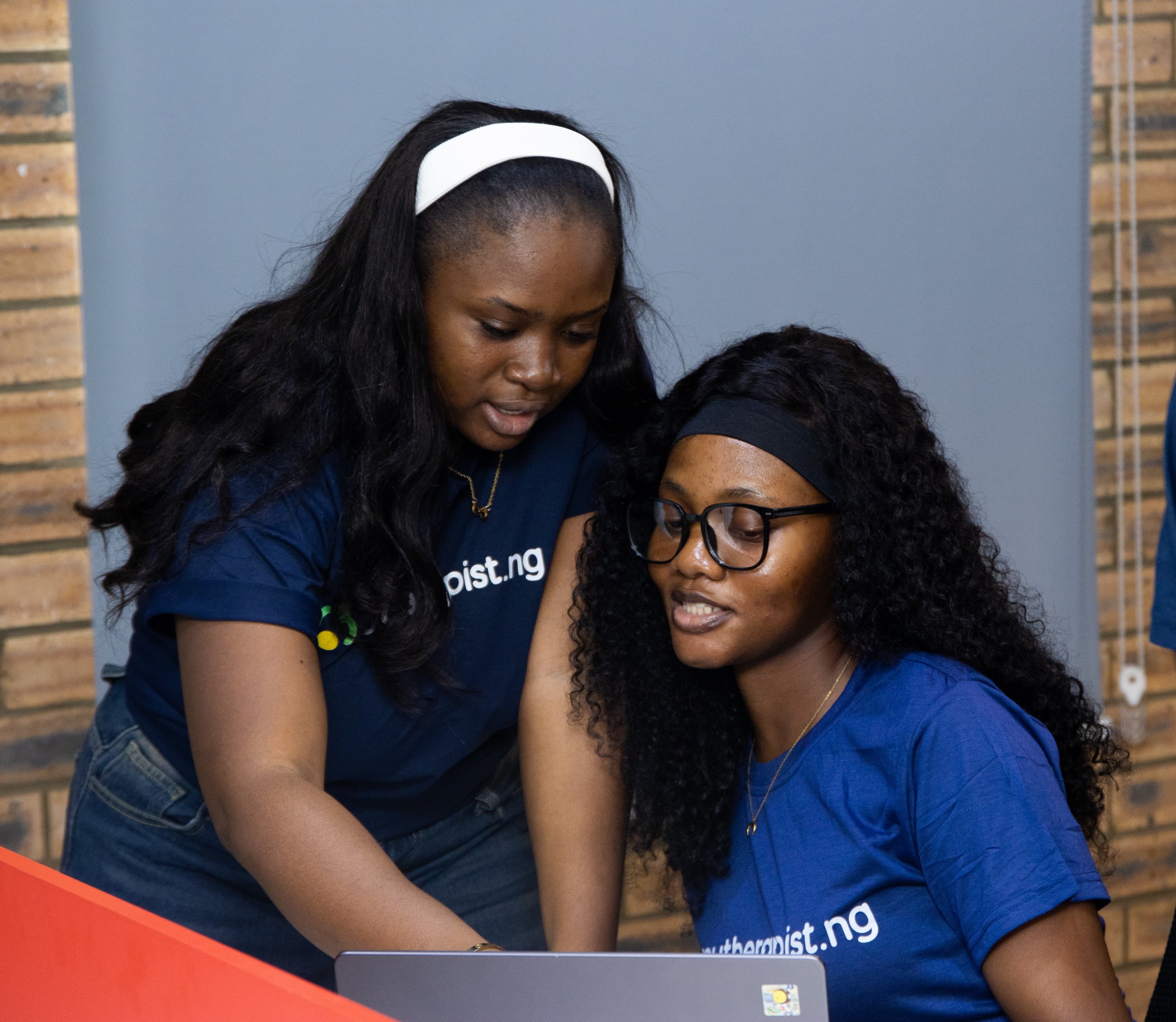Two Mytherapist.ng team members in navy T-shirts looking at a laptop together
