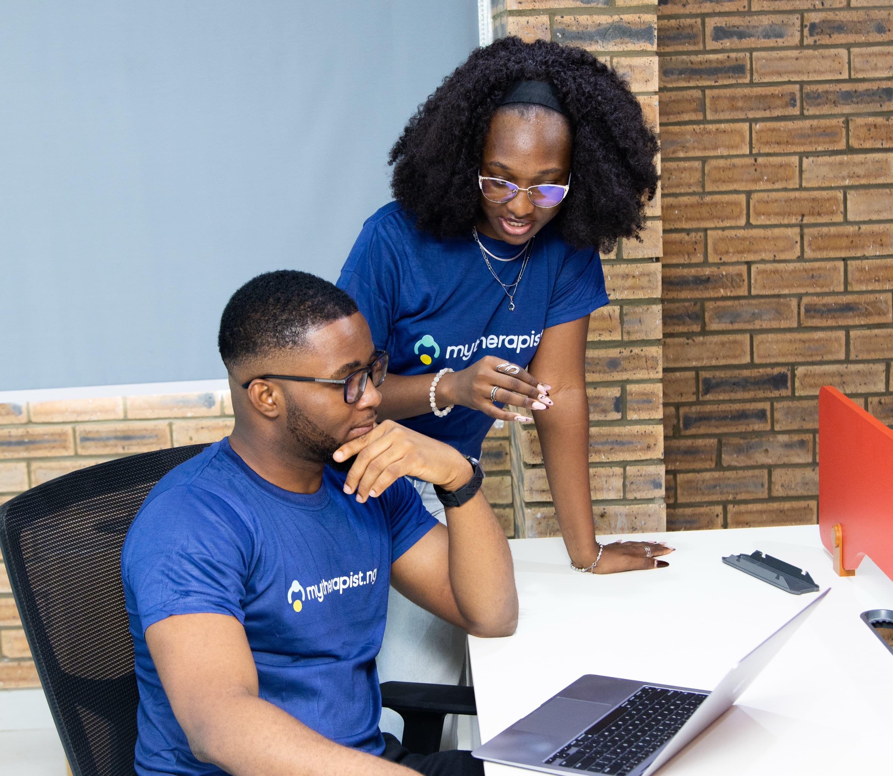 A seated Mytherapist.ng team member and a colleague standing beside him, both looking at a laptop